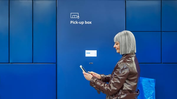 En person i en brun jacka i upphämtningsområdet tittar på sin smartphone.