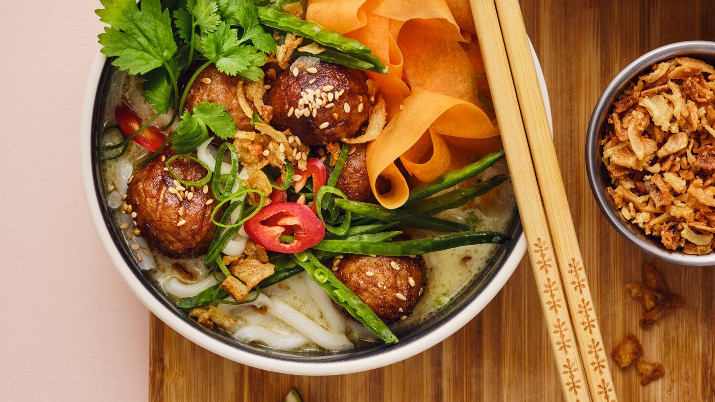 Tre ciotole contenenti pietanze dai sapori asiatici su una superficie in bambù. Su una delle ciotole sono appoggiate delle bacchette.