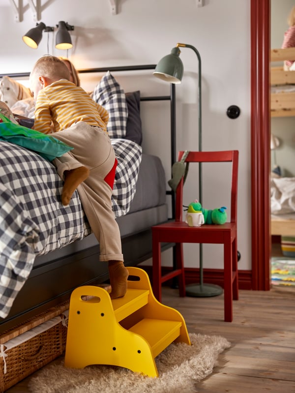 Small child climbing up to parents’ bed on yellow TROGEN children’s step stool. Red wooden chair used as bedside table.