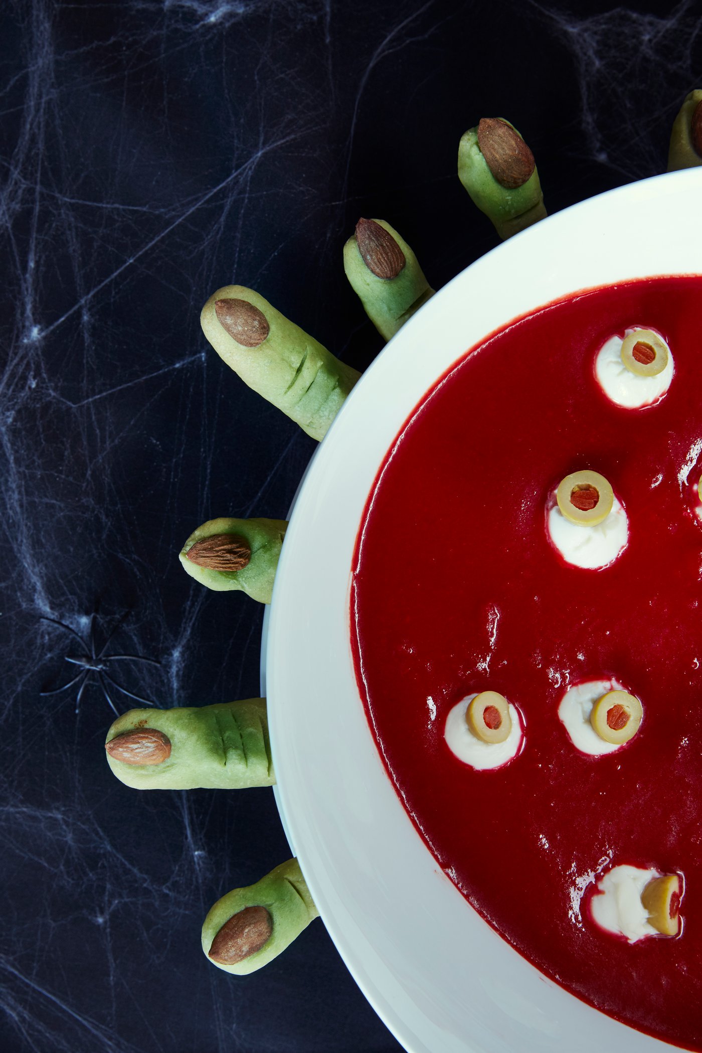 Eine rote Suppe mit Augäpfeln und grünen Marzipanfingern.
