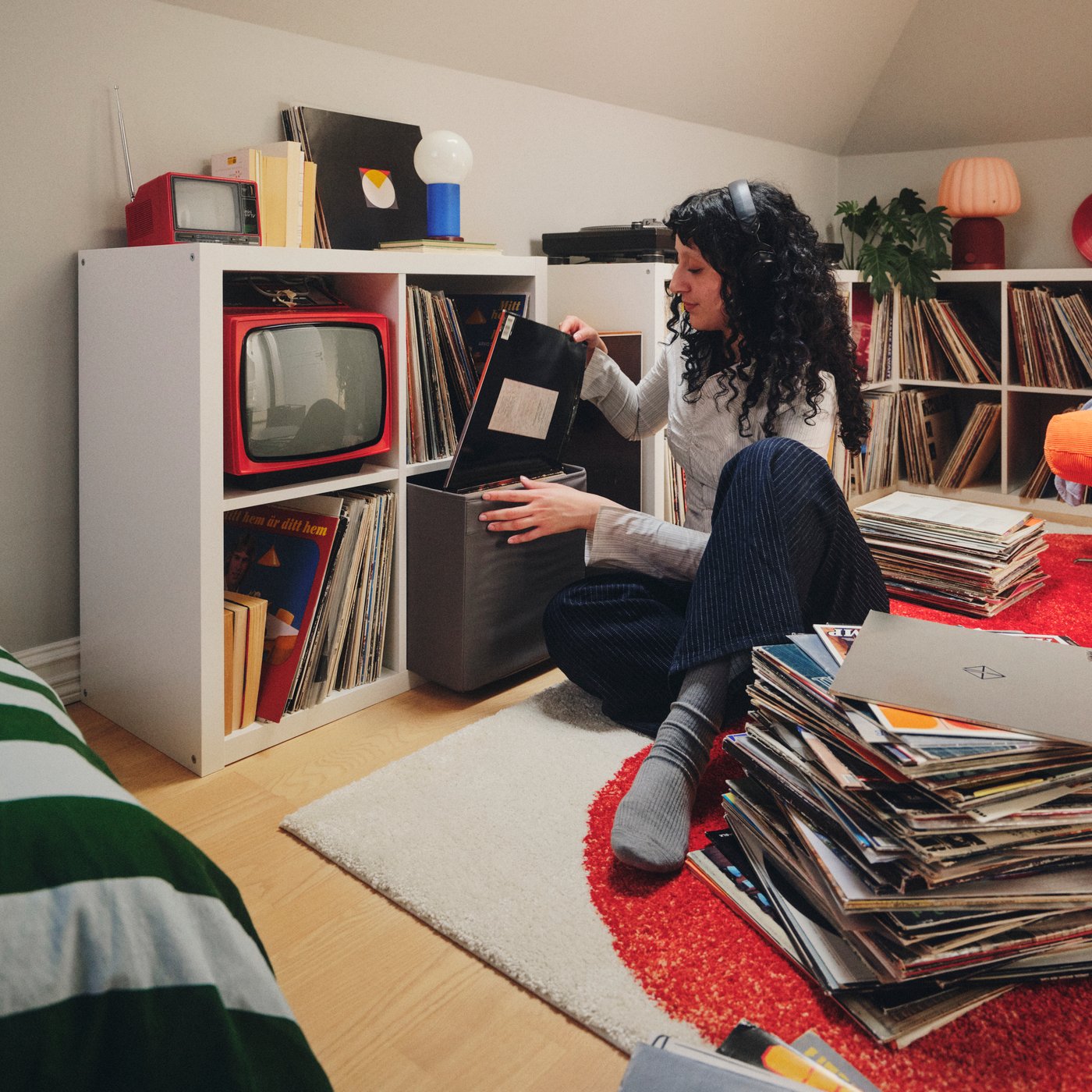 A person wearing headphones puts a record into a storage box that is in a white KALLAX shelving unit with four compartments.