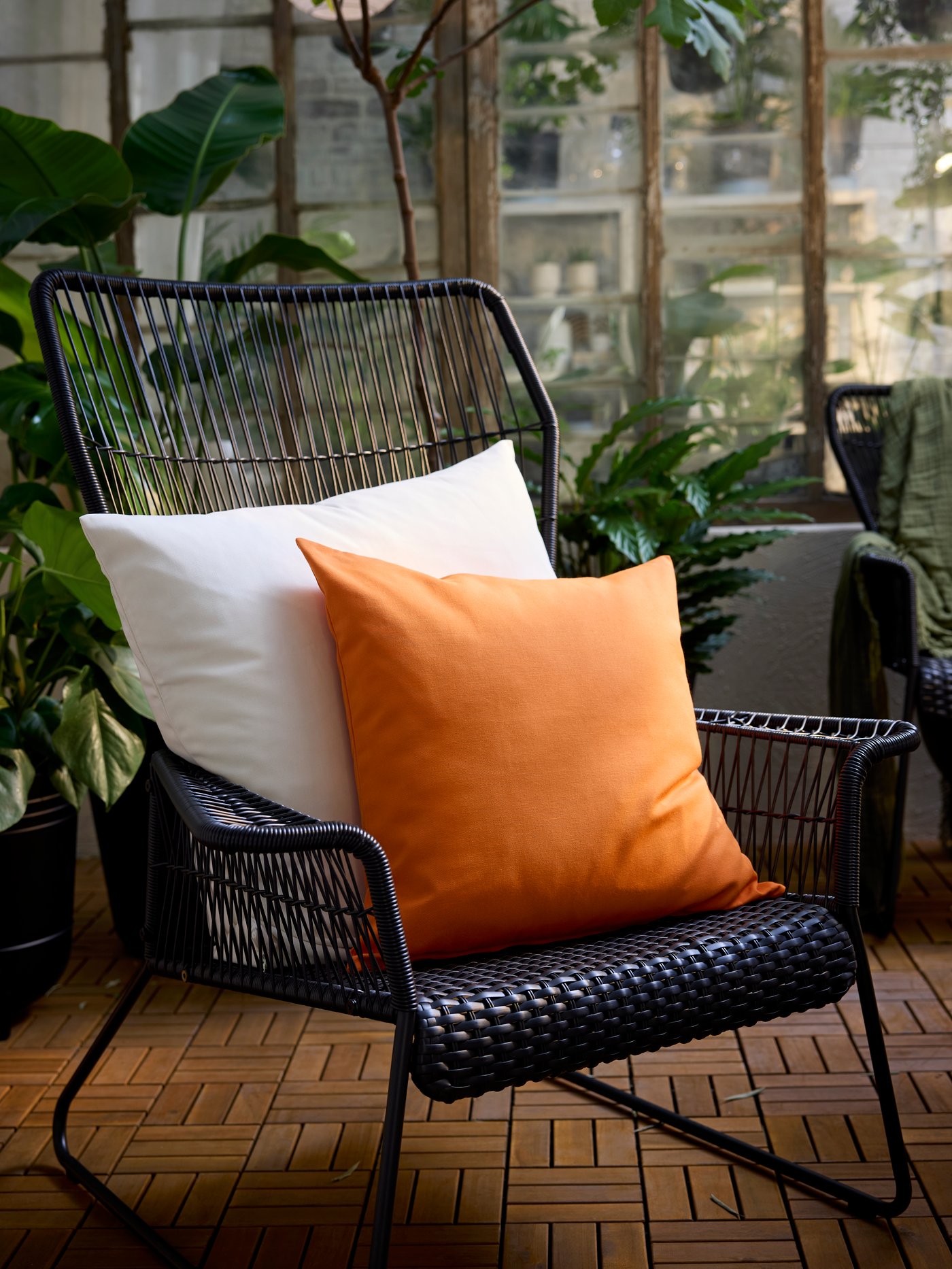 Two cushions with one off-white and one bright orange HJÄRTERÖ cushion cover in a TALLSKÄR chair with armrests on a patio.