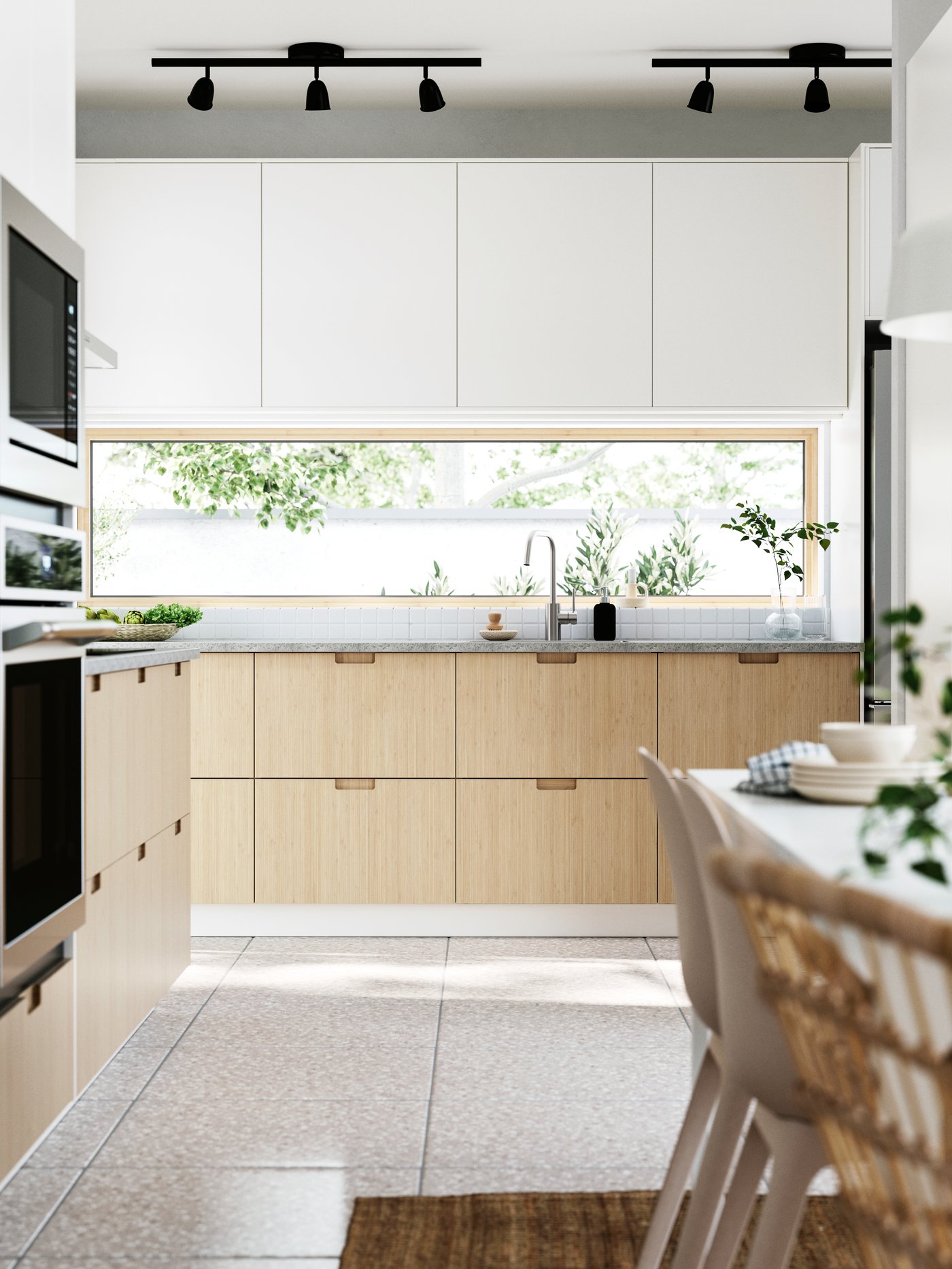A kitchen and dining area with windows facing a garden. FRÖJERED fronts, in bamboo, are combined with VEDDINGE fronts in white.
