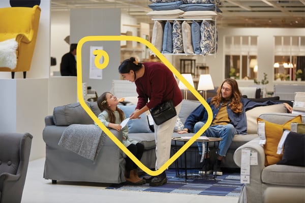 Dans un magasin IKEA, un petit enfant et deux adultes essaient un canapé gris.