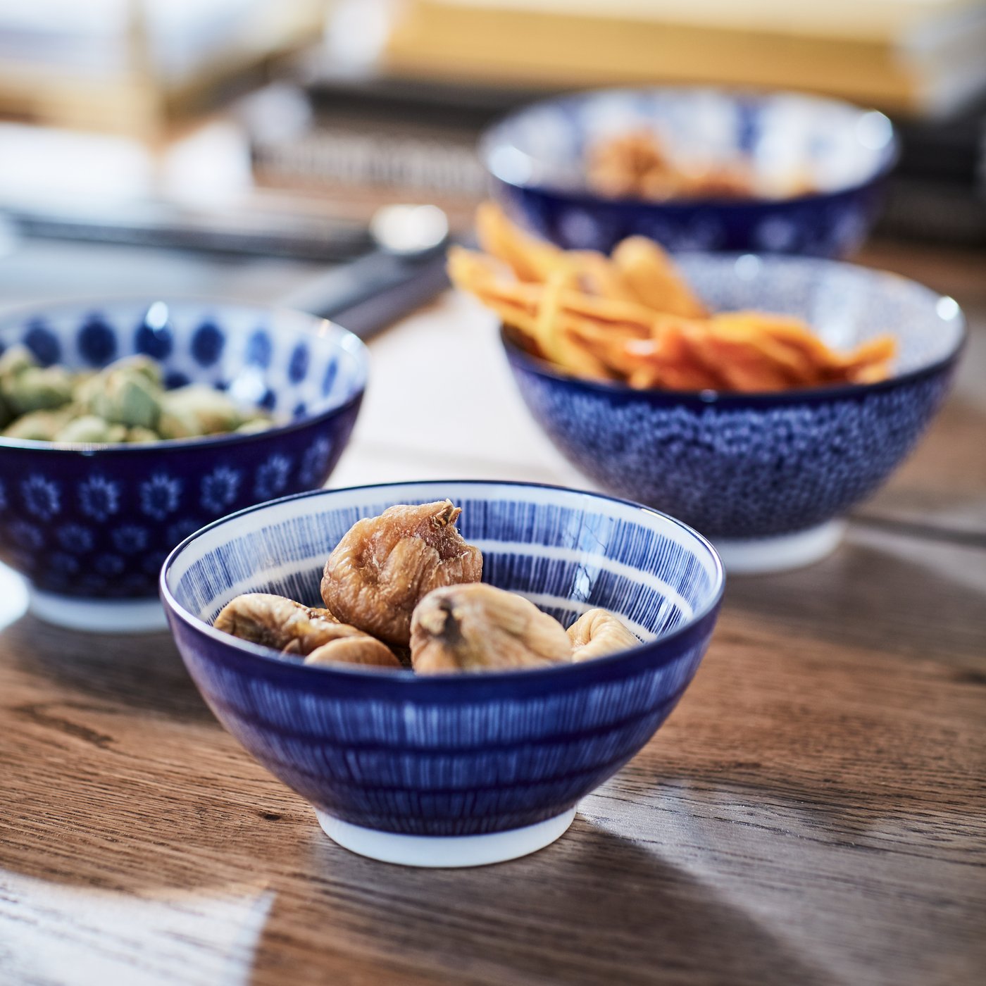 Snacks in four ENTUSIASM patterned, blue bowls on a wooden surface.