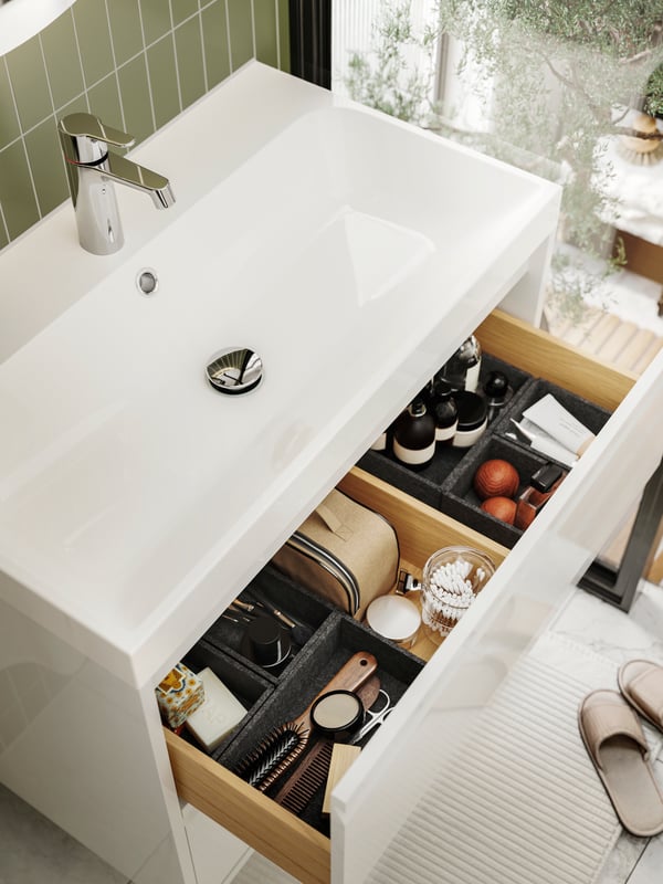 Vue d’en haut d’un lavabo BACKSJÖN dans un meuble lavabo ouvert ÄNGSJÖN à deux tiroirs, dont le premier contient des articles de toilette.