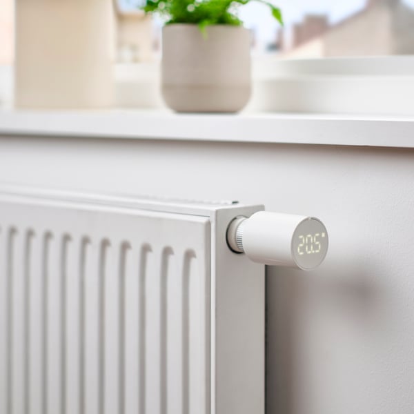 Vit radiator med termostat under ett fönster i ett ljust hem.