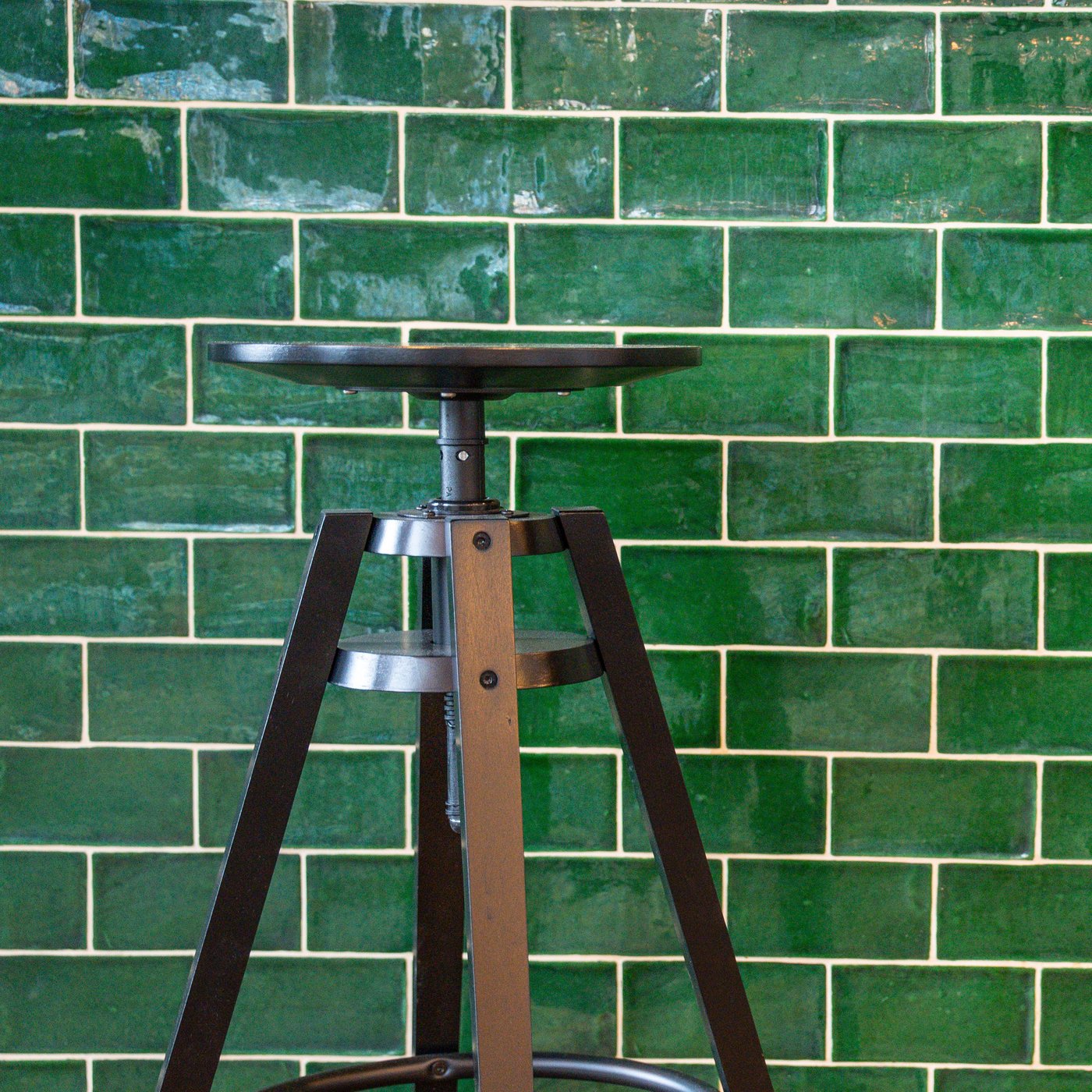Zwarte industriële barkruk voor een muur met glanzende groene tegels in rechthoekig patroon.