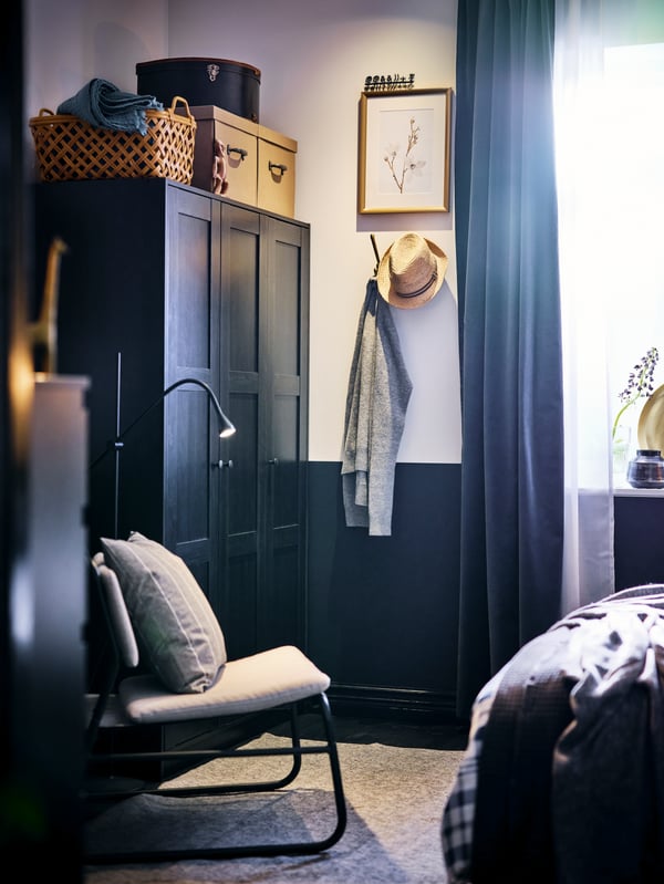 A black brown RAKKESTAD wardrobe with 3 doors in a blue bedroom with a LINNEBÄCK easy chair in Orrsta light grey beside it.