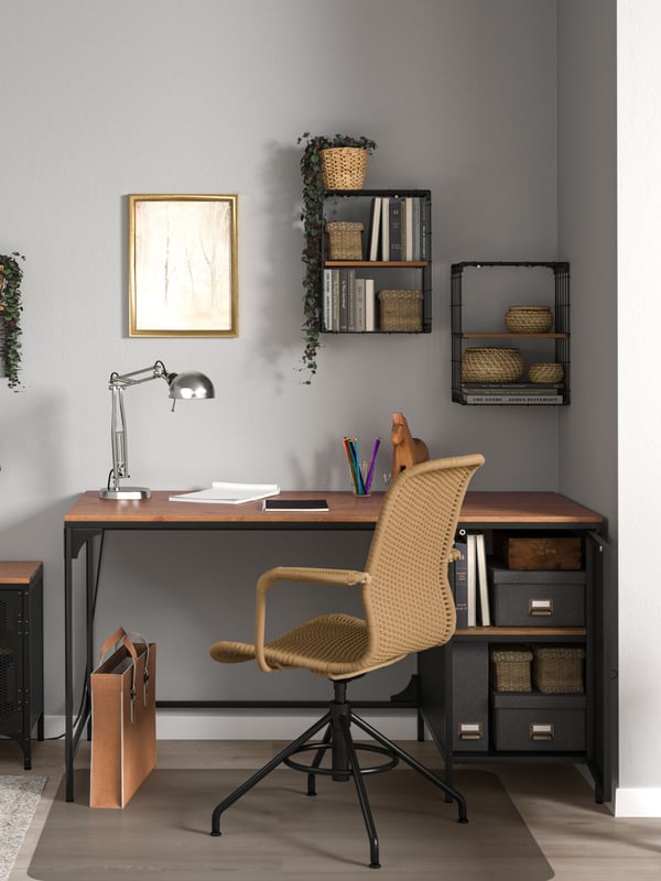 En una estudio hay un escritorio de fierro FJÄLLBO con cubierta de madera con cajas organizadas en sus repisas.