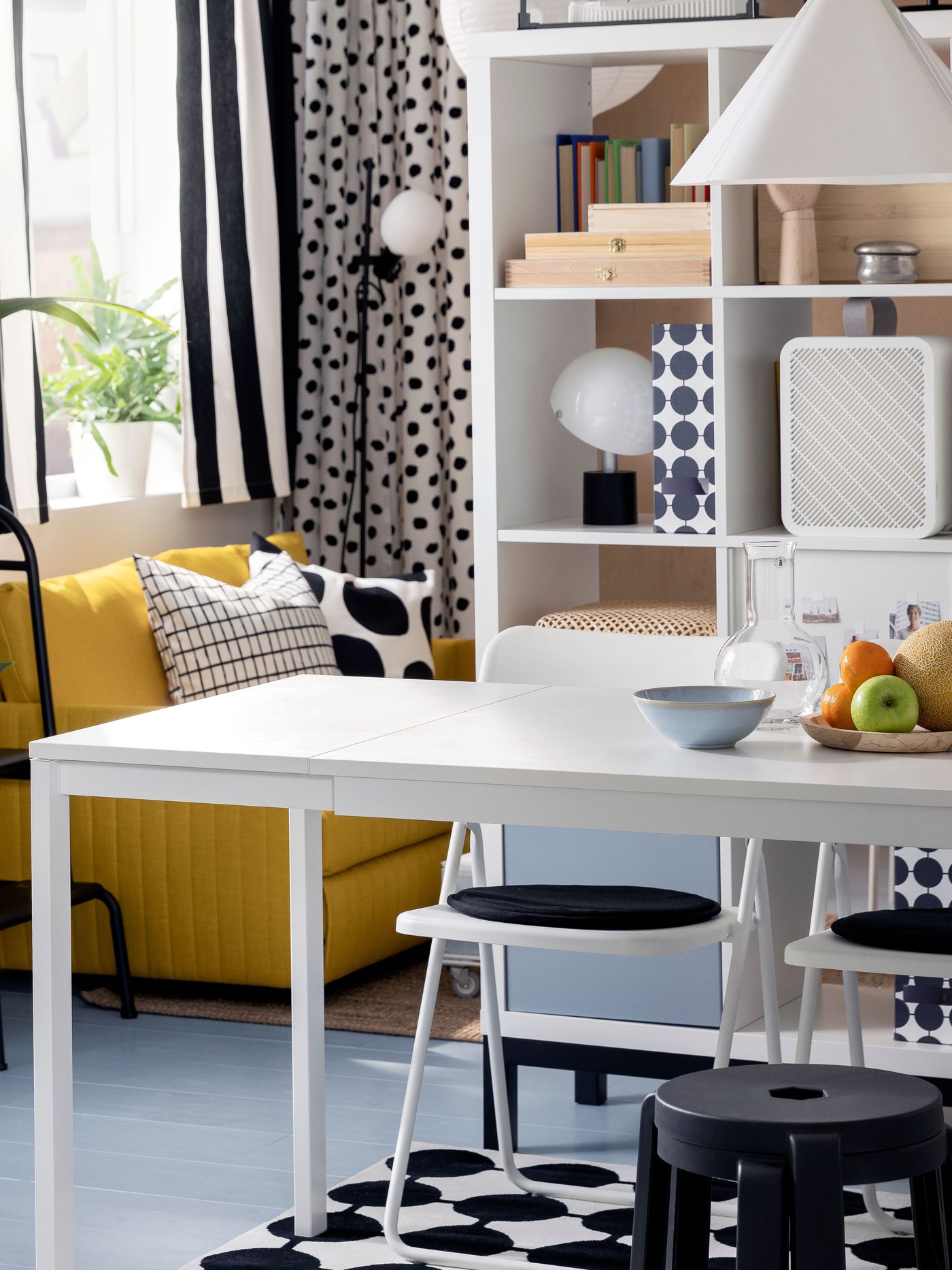 Two stacked, dark grey IBBARBRO stools stand at a white VIHALS extendable table in front of a white KALLAX shelving unit.