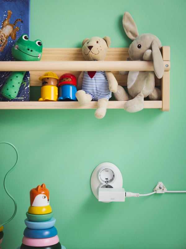 Close-up of FLISAT wall storage full of soft toys such as FABLER BJÖRN and DVÄRGHARE. PATRULL safety plug in socket below.