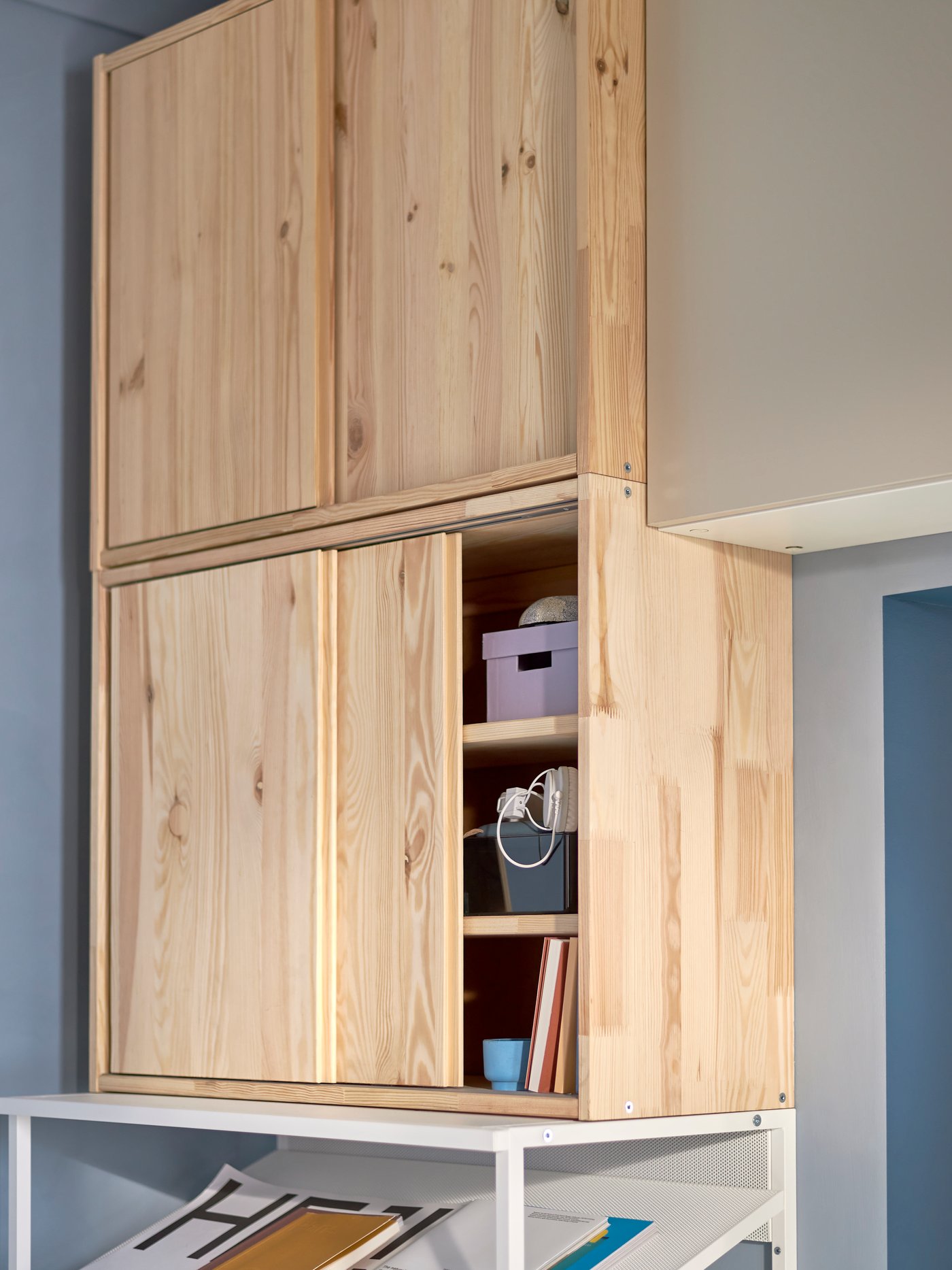 Un mueble IVAR con puertas, una de las puertas está abierta y deja ver el interior del estante con cajas organizadoras.
