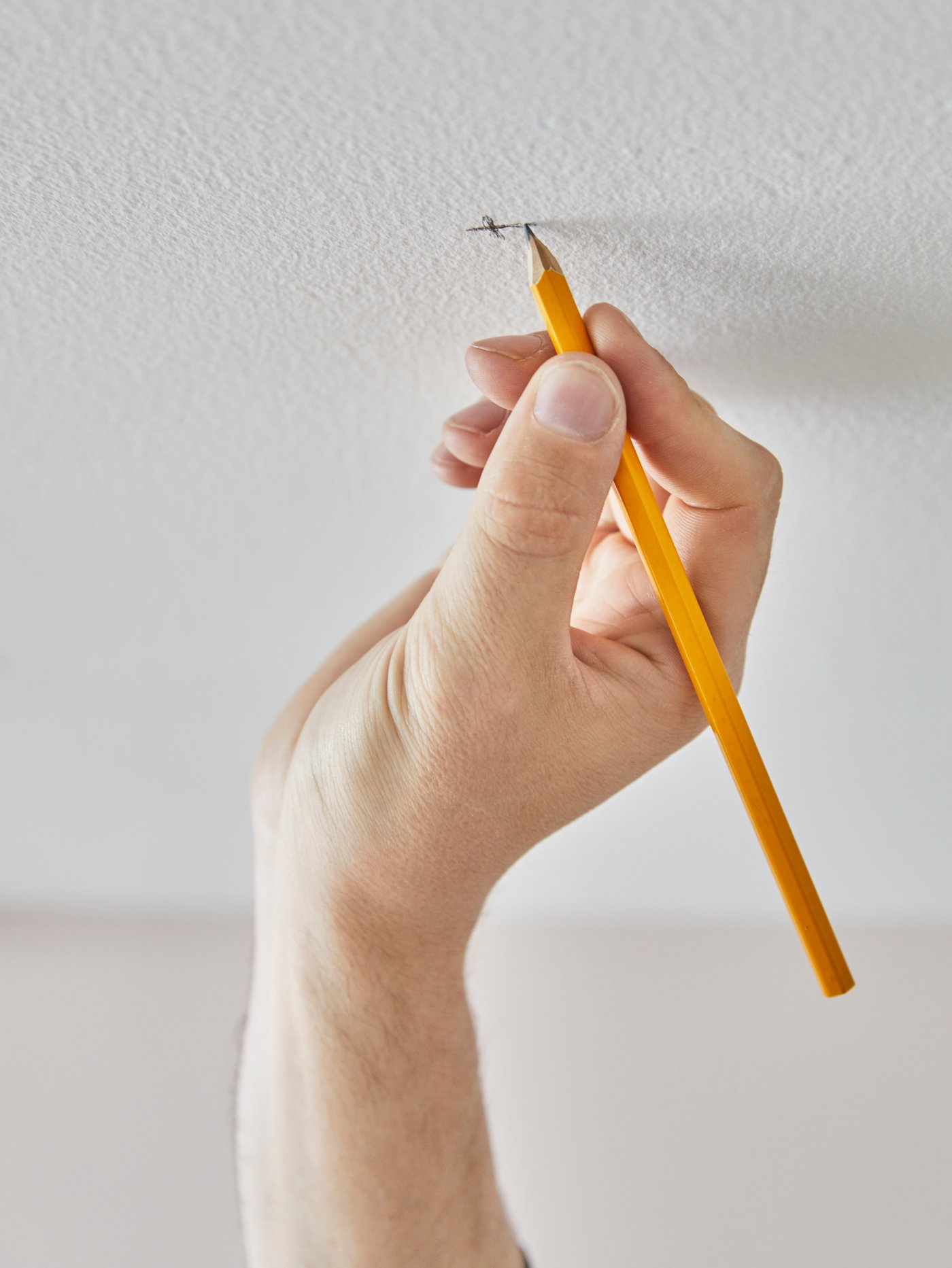 A person’s hand marking a spot on the ceiling for a hole for mounting a VIDGA curtain track rail to the ceiling.