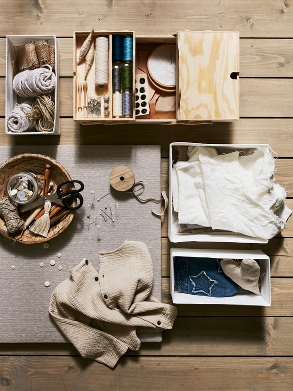 Vista superior de tres cajas SKUBB blancas, un organizador de escritorio KLÄMMEMACKA de madera contrachapada natural y un bowl con accesorios para arreglar la ropa sobre una superficie de madera.
