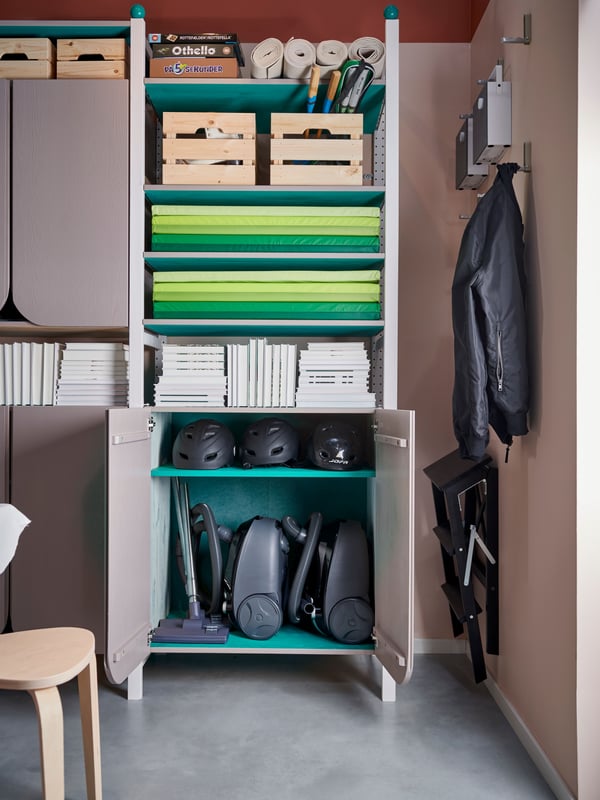 A front view of a open storage unit filled with mats for exercise, wooden boxes, vacuum cleaners and books.
