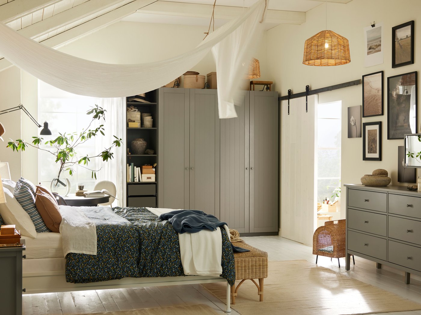 A STJÄRNÖ bed in a bright white bedroom in front of a dark grey/grey PAX/GULLARBERG wardrobe combination and a black table.