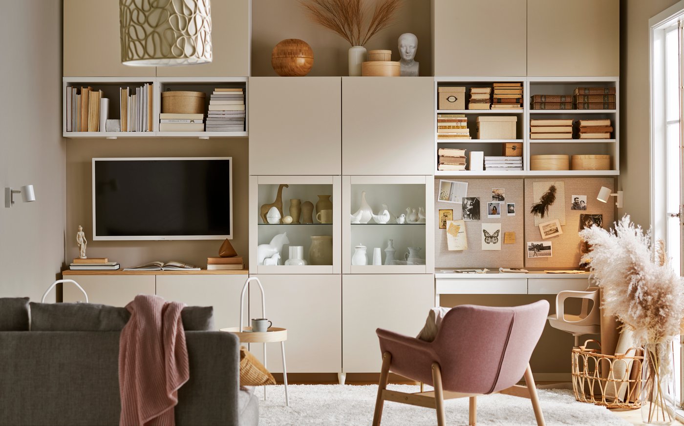 In einem Wohnzimmer sind Kästen an einer Wand mit Deko und Boxen. Auf der linken seite hängt ein Fernseher und davor steht ein Sofa. Auf der rechten Seite kann man einen Stuhl und eine Deko Pflanze sehen.