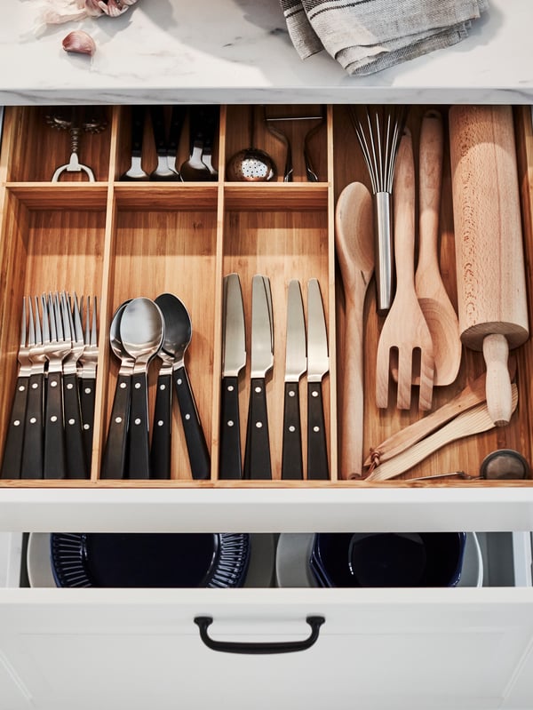 An open kitchen drawer with a VARIERA cutlery tray in bamboo holding cutlery and kitchen utensils inside.