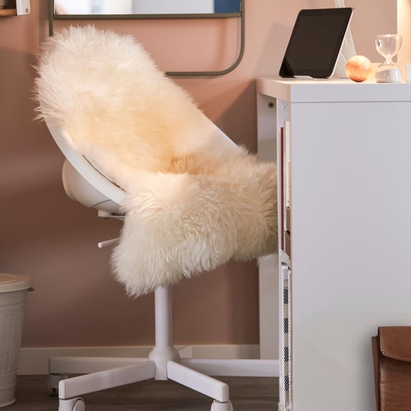 A small home workspace with a white LOBERGET/MALSKÄR swivel chair covered with an ULLERSLEV sheepskin by a white KALLAX desk.