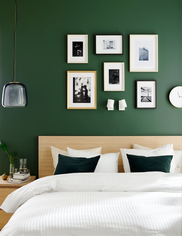 Habitación con decoración de pared sobre una muralla verde, se ven distintos cuadros rectangulares SILVERHÖJD, HOVSTA. Sobre una cama MALM con una funda de edredón NATTJASMIN