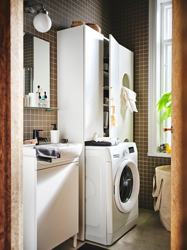 A space holds a NYSJÖN bathroom furniture set, white units for laundry sorting and a STORAVAN soap dispenser.