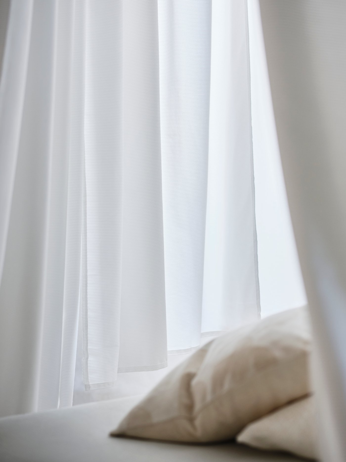 A close-up of the white GUNNLAUG curtains and a tan pillow on a bed.