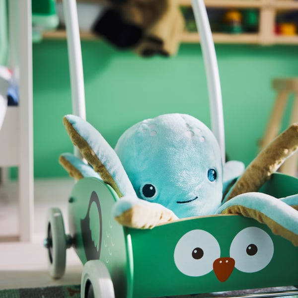 Close-up of UPPSTÅ toddler walker with a light turquoise soft toy octopus in it, and a bright green rug in background.
