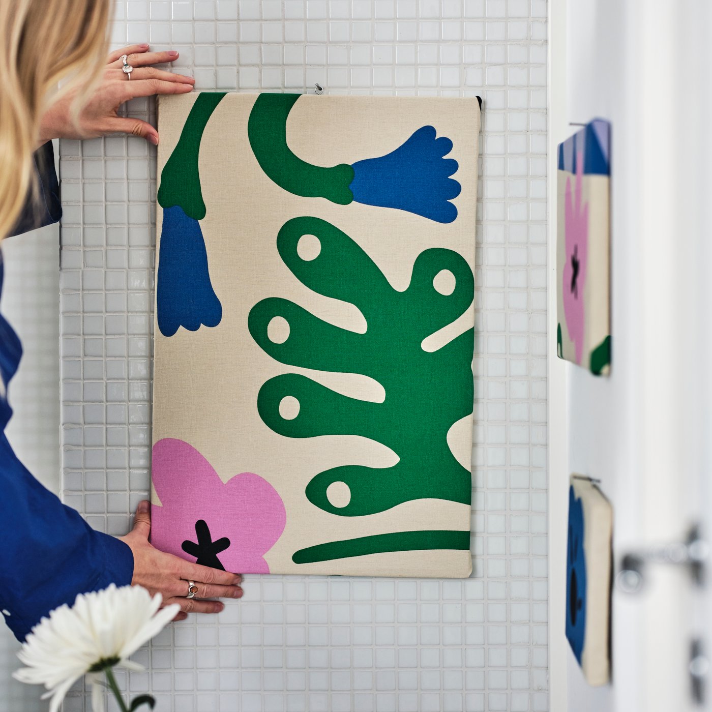 A person adjusts some multicoloured FJÄLLDRABA pre-cut fabric which is being stapled onto a rectangular board.