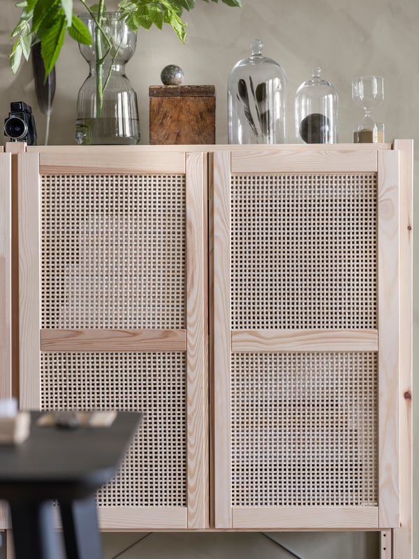 A lattice-fronted wall cupboard with glass vases on top with plant, feathers and other accessories in them.