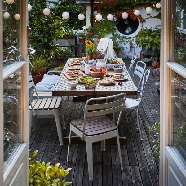 Un p atio con una mesa para exterior NORRMANSÖ con 6 sillas de exterior. Sobre la mesa hay platos de comida.