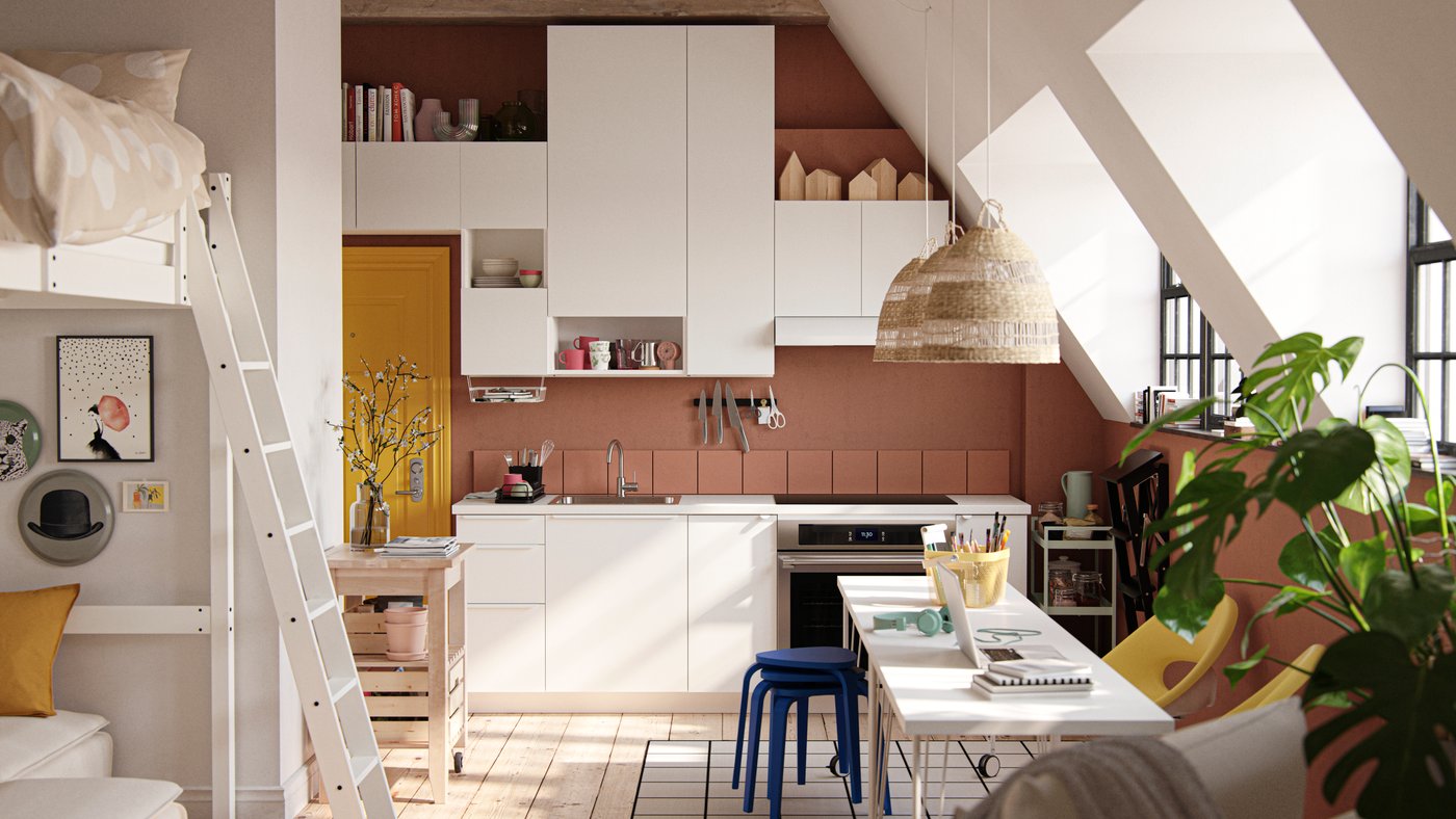 A studio apartment with large industrial-style windows, dark terracotta-colored walls and white VALLSTENA kitchen fronts.