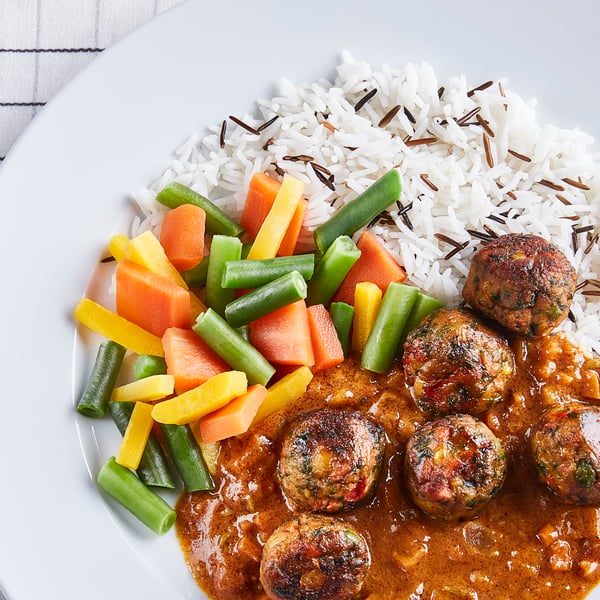 Gros plan d’une assiette avec du riz, des légumes variés et des boulettes de viande dans une sauce épicée, joliment dressée et appétissante.