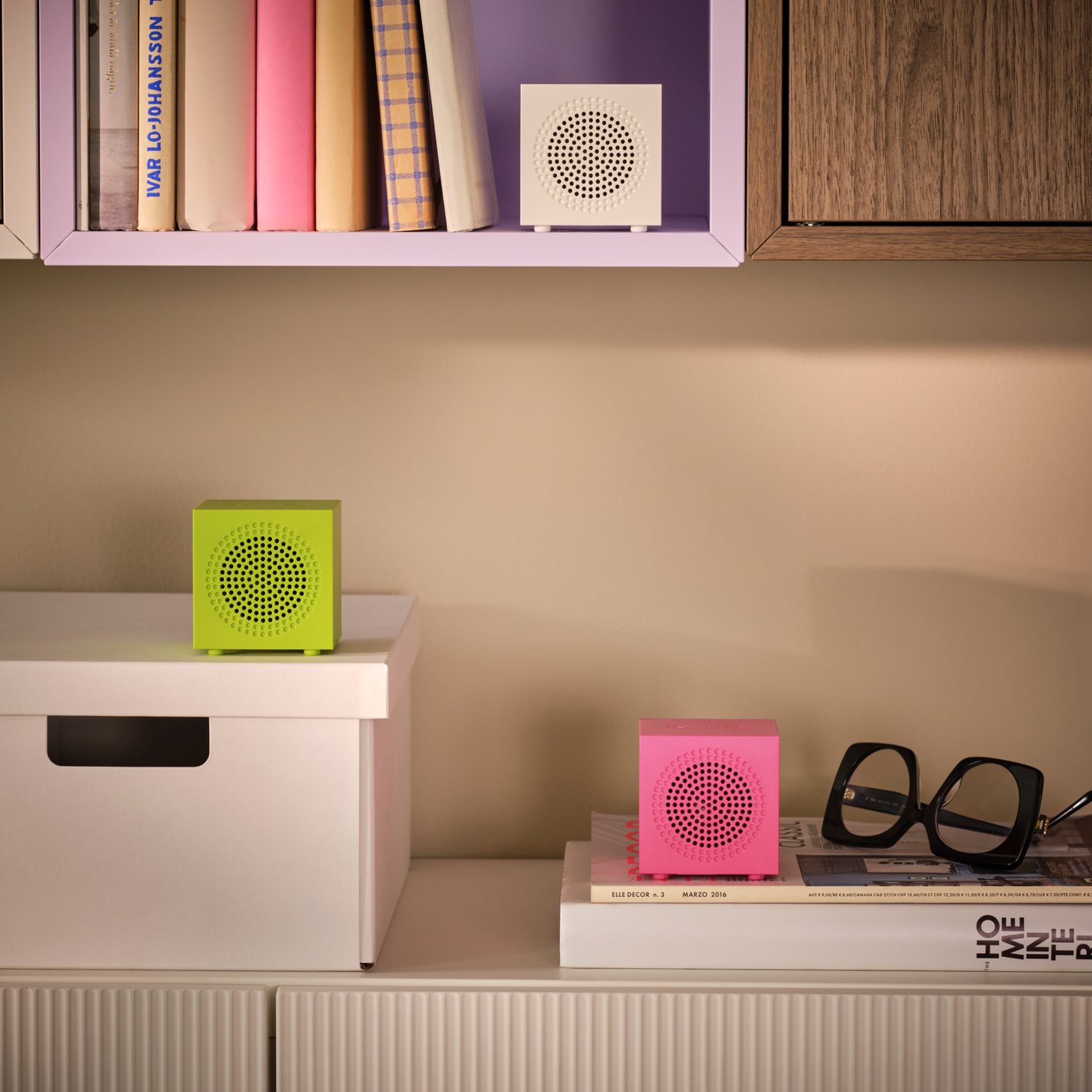 An arrangement of wall cabinets holds books, a box and three KALLSUP portable Bluetooth speakers in different colours.