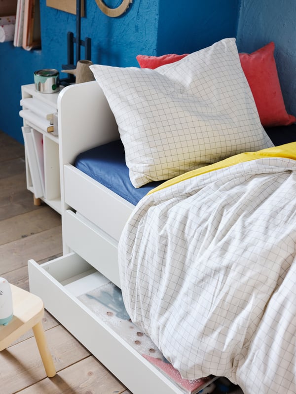 Una cama nido SLÄKT blancacon ropa de cama infantil en tonos blancos. Uno de los cajones de la cama está semi abierto.