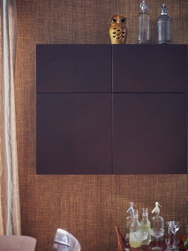 A BESTÅ wall cabinet with HEDEVIKEN doors with an owl and bottles on top, above a dining table holding bottles and glasses.