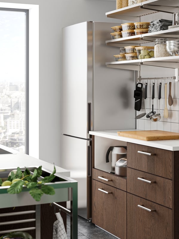 A MEDGÅNG fridge/freezer combination in stainless steel in a kitchen corner with KUNGSFORS shelving in stainless steel.