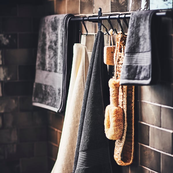 Un cuarto de baño con toallas FREDRIKSJÖN, una toalla y accesorios de baño colgados de ganchos en dos rieles negros HULTARP.