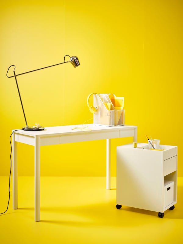 A bright yellow space with a TONSTAD desk and TONSTAD drawer unit on castors. There is a black lamp on the desk.