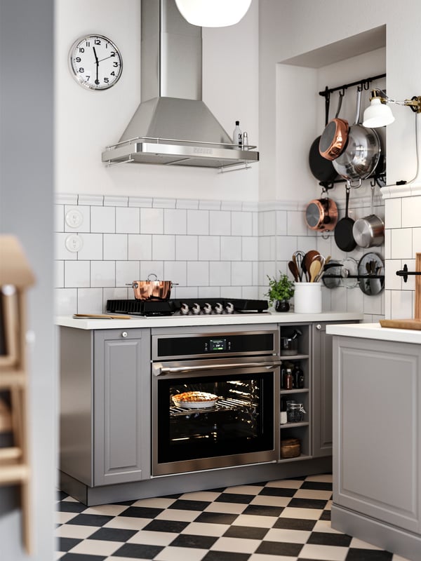 Base cabinets with grey BODBYN kitchen fronts on both sides of a hob and oven, plus black wall rails holding pots and pans.