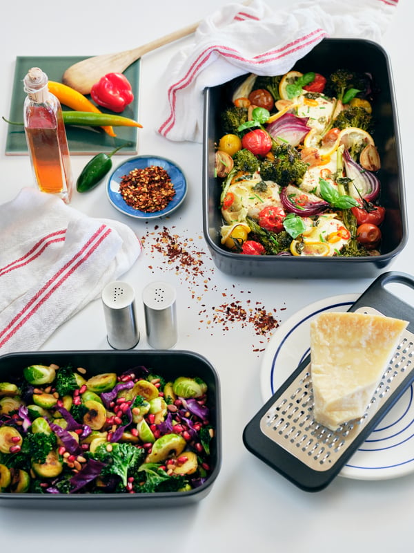 Un plateau blanc avec de la nourriture colorée sur un plat à four LYCKAD gris foncé, entouré d'accessoires de cuisine.