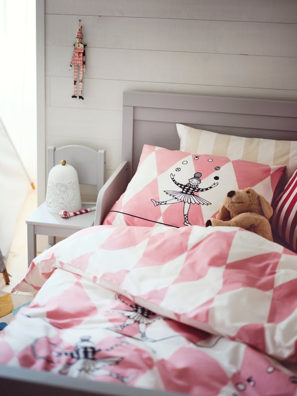 Dans une chambre d’enfant, un chien en peluche GOSIG GOLDEN couché sur l’oreiller dans un lit extensible SUNDVIK gris avec du linge de lit BUSENKEL.