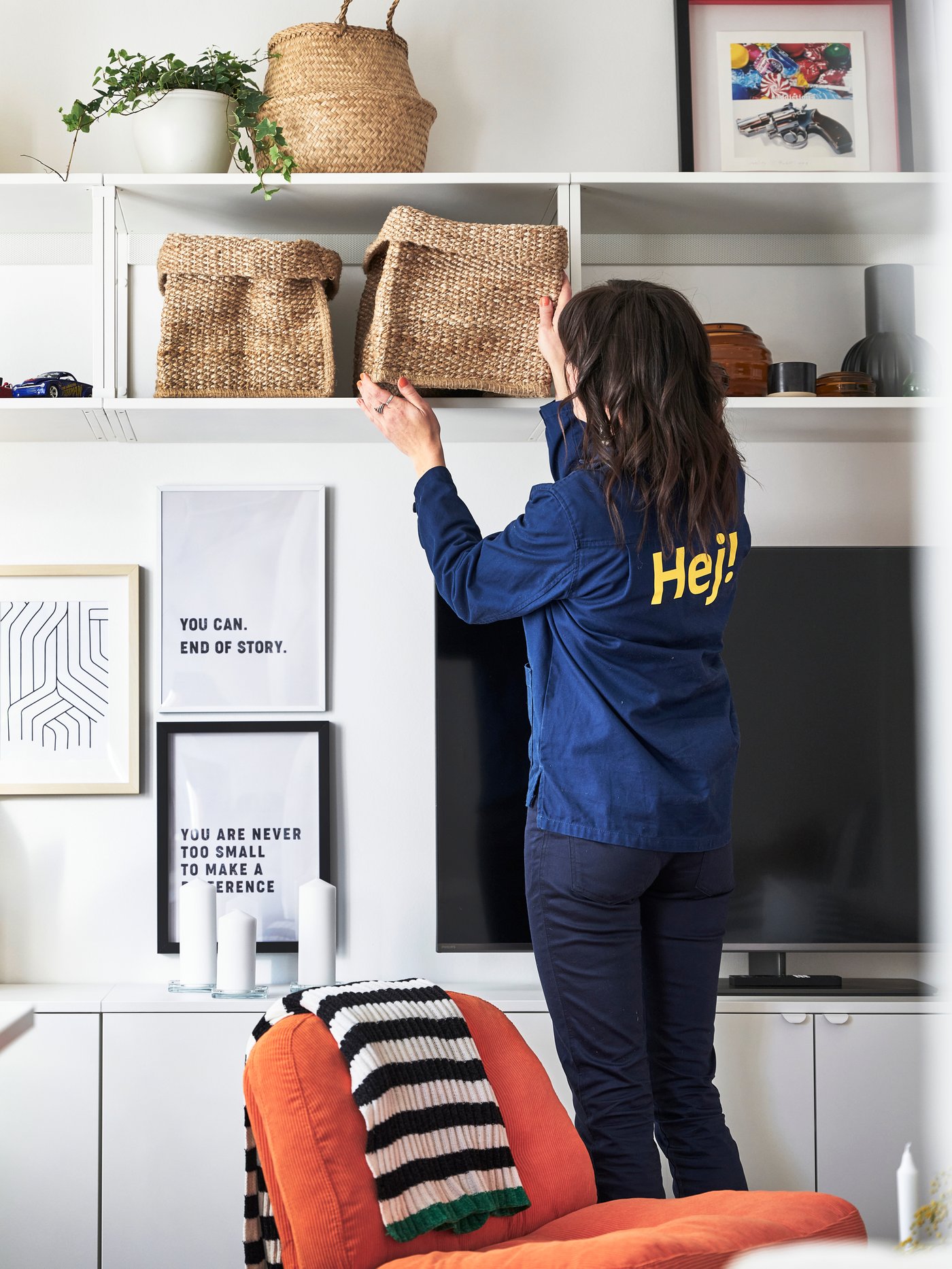 En IKEA inredare plockar ner en flätad förvaringskorg från en vägghylla i en liten etta som hon inrett.