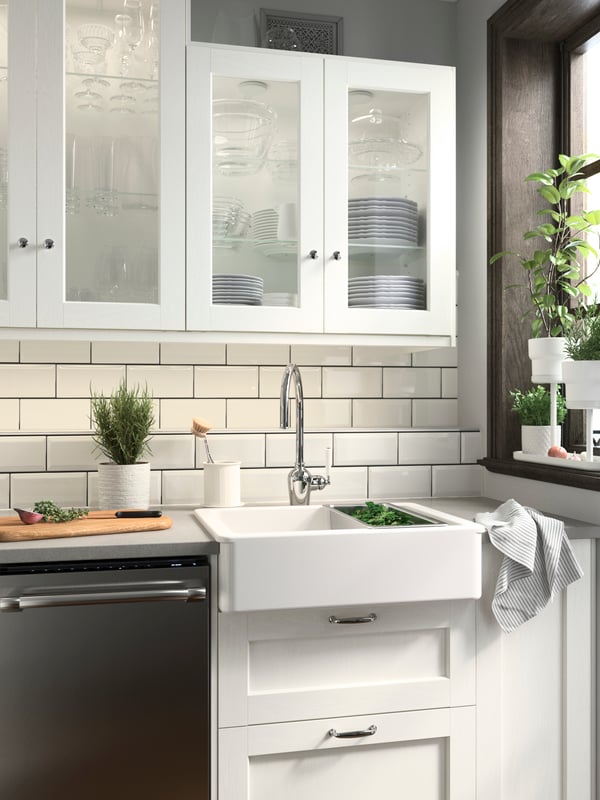 A kitchen with ENKÖPING white fronts, a white HAVSEN sink bowl, wall storage and white plant pots with green herbs growing.