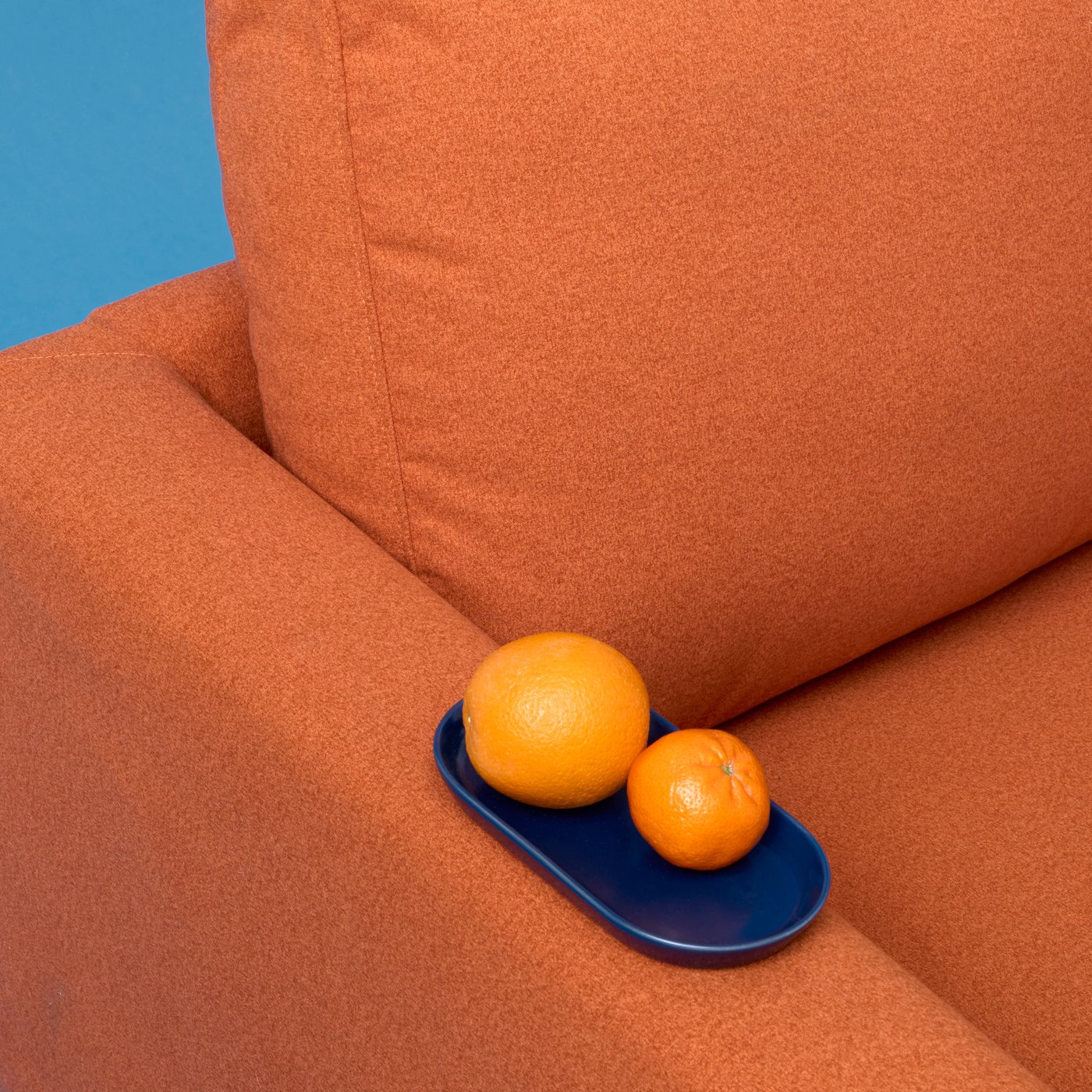 An orange and a clementine on a blue dish placed on the armrest of a Tonerud red-brown SALTSJÖBADEN three-seat sofa.