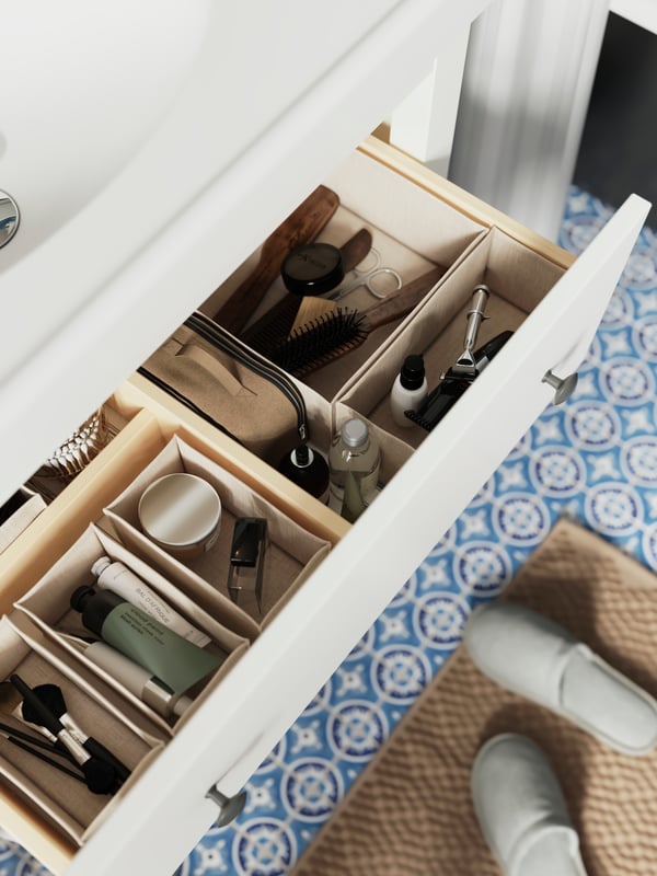 A drawer in a white HEMNES wash-stand is pulled out and there are interior organisers inside with bathroom products in them.