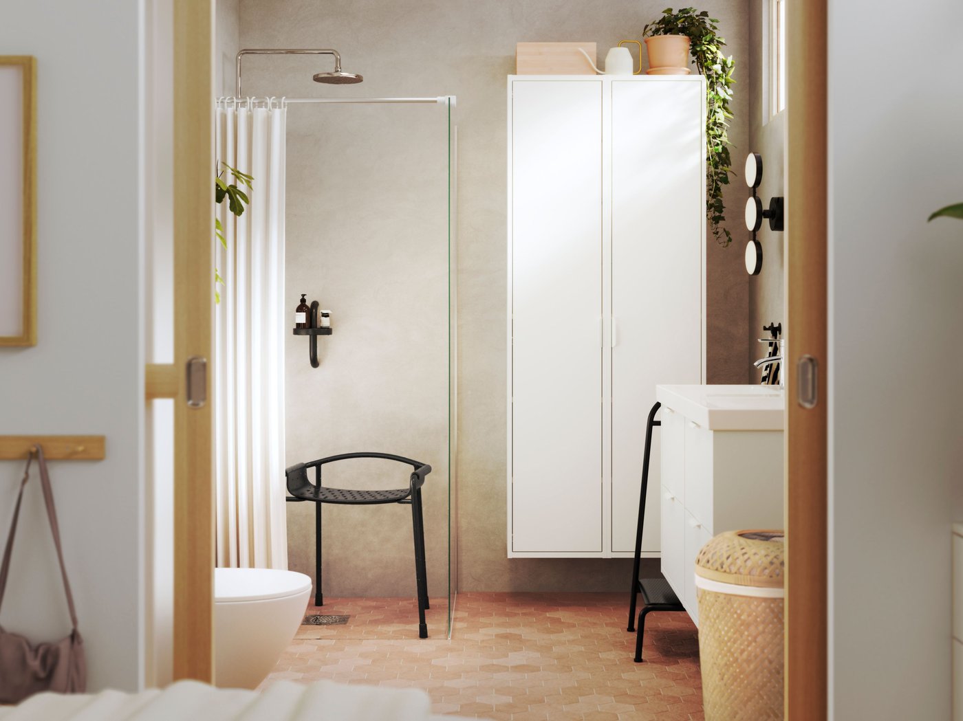 A bright bathroom is seen from a bedroom, and it has white HAVBÄCK bathroom furniture and BÄSINGEN accessories in anthracite.