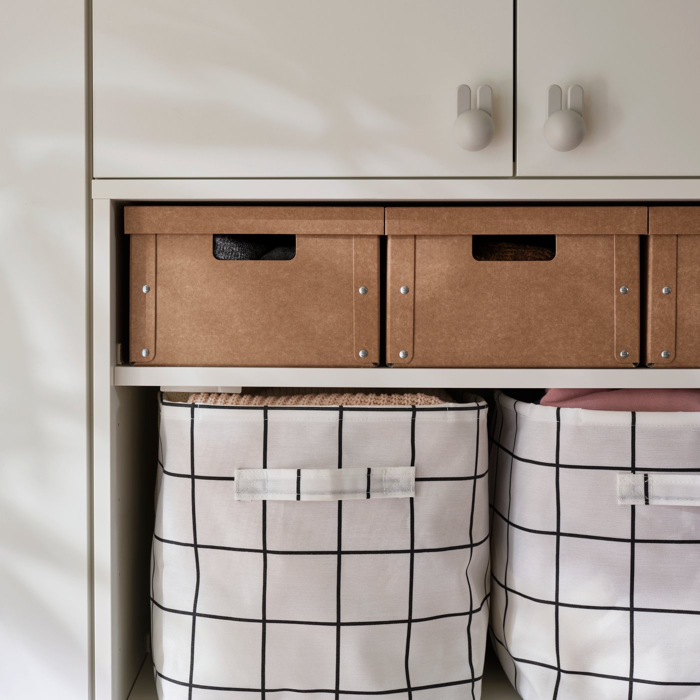 A shelving unit holding GÄRDESGÅRD big boxes with lids placed above large patterned fabric bins in a hallway.