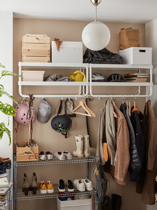 Two white hat and coat racks hanging on a beige wall with jackets, hats, helmets, bags and boxes on it.