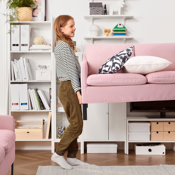 One person carrying one end of a pink sofa through a living room; the person carrying the other end is out of shot.